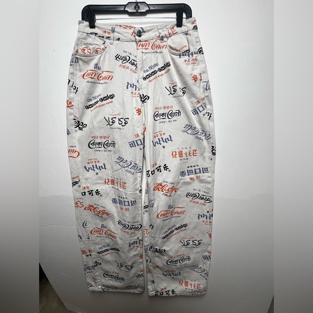 COCA-COLA CREAM JEANS FEATURING ALL-OVER COKE LOGOS IN VARIOUS LANGUAGES. SIZE 6